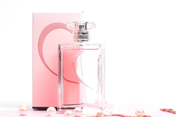 Różowa butelka perfum z perłami i złoty łańcuszek na odwrocie pudełka na różowym prześcieradle na białym tle. widok na bot, orientacja pozioma — Zdjęcie stockowe