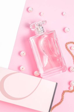 İnci ve altın zincirli pembe parfüm şişesi ve beyaz arka plan fotokopi alanındaki pembe çarşafın üzerinde bir kutu. Üst görünüm, model