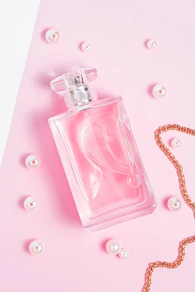 Garrafa de perfume rosa com pérolas e uma corrente de ouro em uma folha rosa em um espaço de cópia de fundo branco. vista superior, mockup — Fotografia de Stock