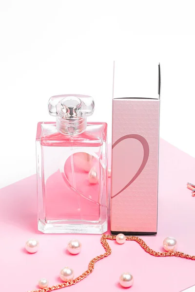 Garrafa de perfume rosa com pérolas e uma corrente de ouro e uma caixa de lado em uma folha rosa em um espaço de cópia de fundo branco. bot view, orientação vertical — Fotografia de Stock