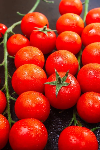 Dois ramos maduros de tomates de cereja em baixas de água de Ross em uma mesa gravada preta. espaço de cópia, close-up, orientação vertical — Fotografia de Stock