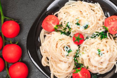 Siyah tabakta siyah bir masada ıspanaklı, domatesli, susamlı ve peynirli spagetti. Kapat, boşluğu kopyala, üst görünüm