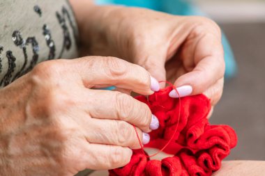 Yaşlı kadın elleri kırmızı bir bezi iğneyle dikiyor.