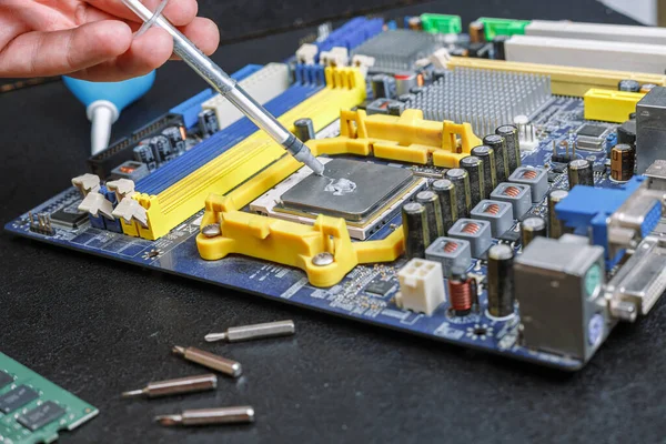 Computer moederbord hand knijp thermisch vet uit een spuit, reparatie apparatuur op de tafel — Stockfoto