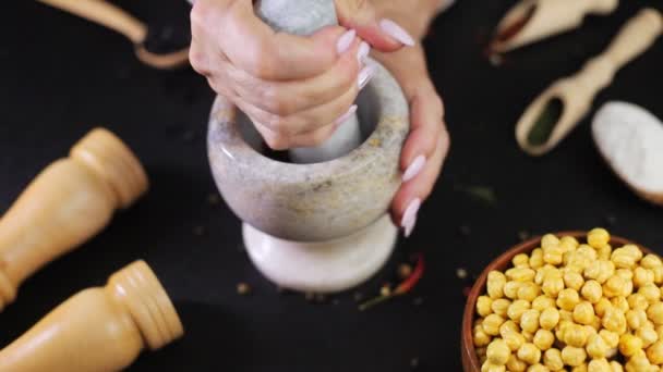 As mãos femininas moem uma argamassa de pedra com pimenta e colheres de madeira com especiarias na mesa — Vídeo de Stock