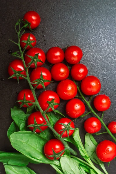 Dvě zralé cherry rajčatové větve se špenátem na černém reliéfním stole. kopírovat prostor, horní pohled, byt ležel — Stock fotografie