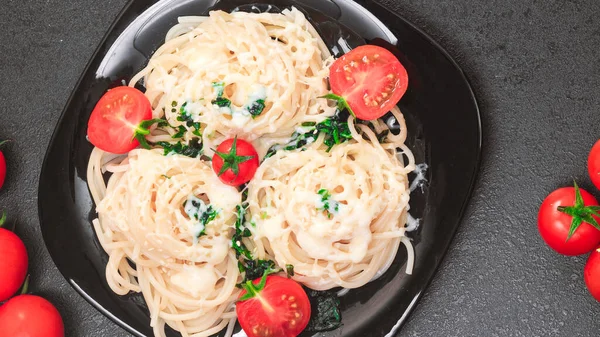 Špagety se špenátem, rajčaty, sezamovými semínky a sýrem na černém stole na černém talíři. plochá poloha, kopírovací prostor, horní pohled — Stock fotografie