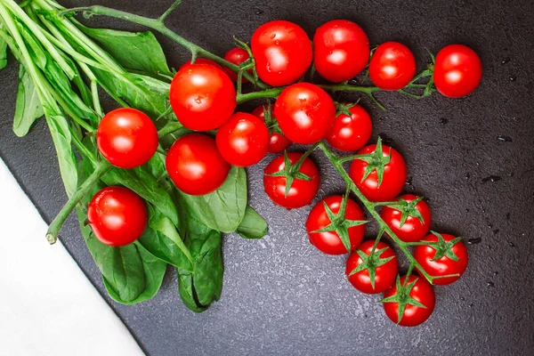 Due rami maturi di pomodorini e un asciugamano di lino bianco con spinaci su un tavolo nero goffrato. spazio di copia, vista dall'alto, disposizione piatta, orientamento orizzontale — Foto Stock