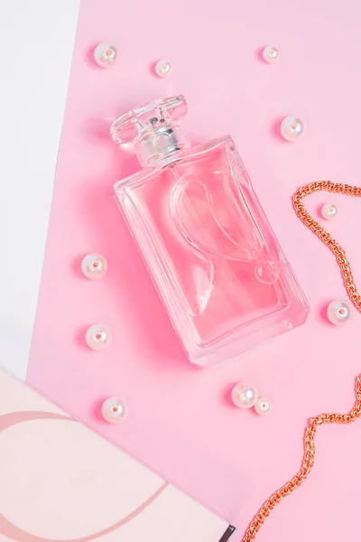 ピンクの香水瓶に真珠と金の鎖と白い背景のコピースペースのピンクシートの箱。トップビューモックアップ — ストック写真