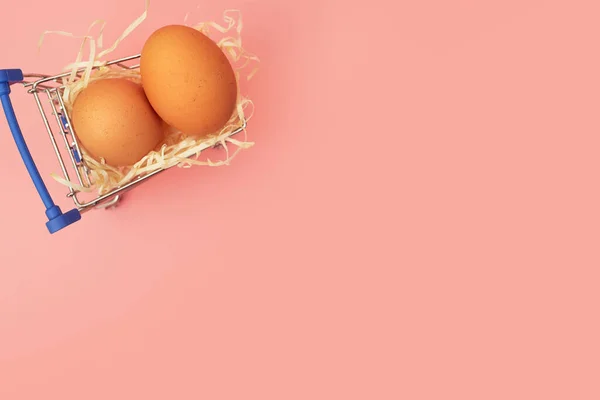 Kyckling ägg i en kundvagn på en rosa pastell bakgrund, kopiera utrymme, flatlay — Stockfoto