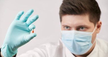 Coronavirus kavramı, beyaz arka planda kapsülleri olan tıbbi maskeli adam.