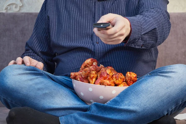 Adam kanepede bir tabak tavuk kanadı ile televizyon izliyor.