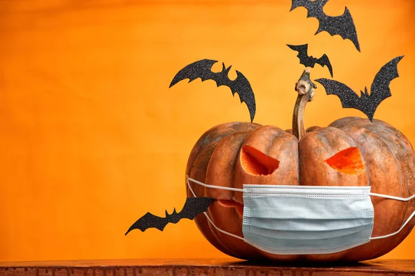 Zucche di Halloween in una maschera medica e pipistrelli su uno spazio di copia di sfondo arancione — Foto Stock