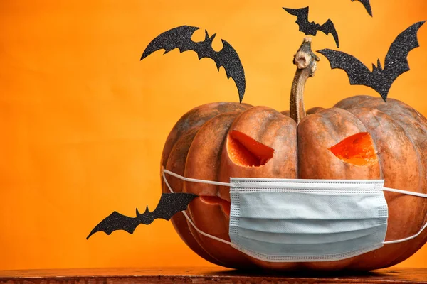 Zucche di Halloween in una maschera medica e pipistrelli su uno spazio di copia di sfondo arancione — Foto Stock