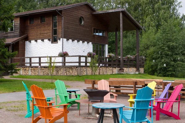 Campfire field with colorful chairs and a house in the background.