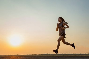 Gün batımında koşan ve egzersiz yapan genç kadınların silueti. Arka planda güneş, renkli günbatımı semalarıyla.