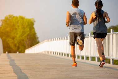 Gün batımında koşan ve egzersiz yapan bir çiftin silueti. Arka planda güneş, renkli günbatımı semalarıyla.