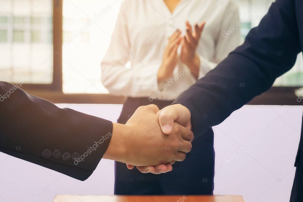 Business people shaking hands at meeting while theirs colleagues clapping and applauding. Success teamwork, partnership and handshake