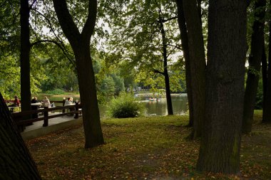 Parktaki göl her yönden ağaçlarla çevrilidir. Gölde insanlar kayıklarla yüzer..