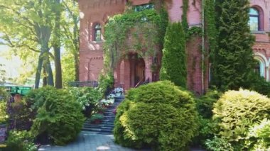 Rusya 'nın Kalininingrad şehrinde güneşli bir bahar gününde, bahçesine tırmanma bitkisi ve çiçek döşenmiş kırmızı tuğla duvarlı eski lüks özel evin giriş kapısı..