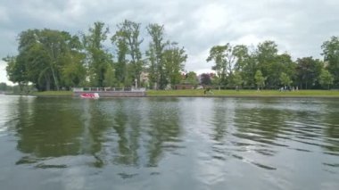 Yukarı Göl 'de boş bir kayık - yapay şehir göleti, ünlü turistik eğlence merkezi ve Rusya' nın Kalininingrad şehrinde bulutlu bir bahar gününde popüler dinlenme alanı. 4K 'da gösterilen düşük açılı panoramik görünüm