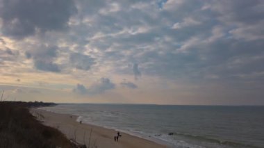 Rusya 'nın Kaliningrad Oblastı' ndaki popüler sahil beldesi Zelenogradsk 'ta bulutlu bir bahar gününde birkaç turistle Baltık Denizi kıyısında bir kumsal gezintisi. 4K 'da çekilen yüksek açılı atış