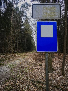 Yeşil bir ormanın önündeki asfaltsız yolda trafik uyarı levhası