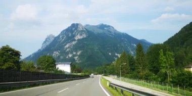 Gökyüzünde parlak bir güneş sıcak bir yaz gününde parlar iken Avusturya Alpleri yol üzerinden araba yolculuğu.