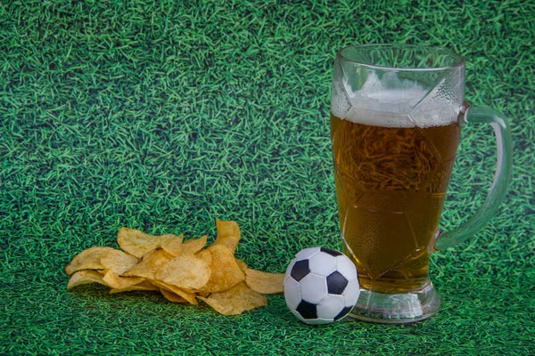 beer glass with beer,  chips, soccer ball \football on a background of green grass