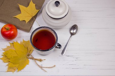 Beyaz bardakta çay, beyaz şeker ve kamış şekeri, akçaağaç yaprağı ve elmalar ahşap arka planda..