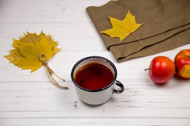 Beyaz bardakta çay, beyaz şeker ve kamış şekeri, akçaağaç yaprağı ve elmalar ahşap arka planda..