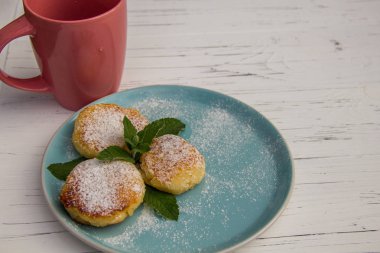 Mavi tabakta cheesecake ve açık ahşap arka planda pembe kupa kahve.