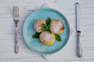 Çatal ve bıçaklı mavi tabakta cheesecake, hafif ahşap zemin üzerinde pamuk bez