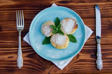Çatal ve bıçaklı mavi tabakta cheesecake, kahverengi ahşap arka planda pamuk bez.