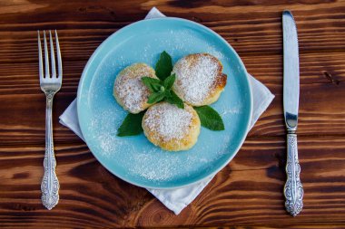 Çatal ve bıçaklı mavi tabakta cheesecake, kahverengi ahşap arka planda pamuk bez.