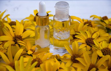 Sarı çiçekler ve beyaz kozmetik krem şişede ve ahşap bir arka planda tonik