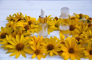 Sarı çiçekler ve beyaz kozmetik krem şişede ve ahşap bir arka planda tonik