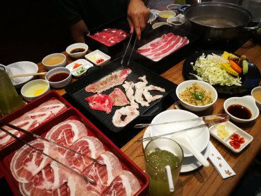 İnsanlar bir restoranda shabu ya da ızgara et yiyor.