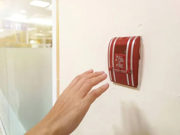 The hand of man is pulling fire alarm on the wall