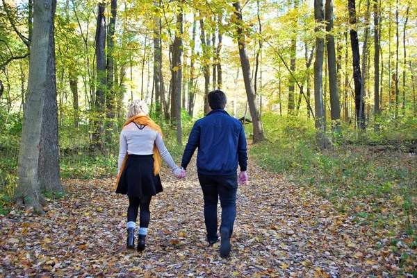 A young couple walking down a trail in the woods holding hands in the fall