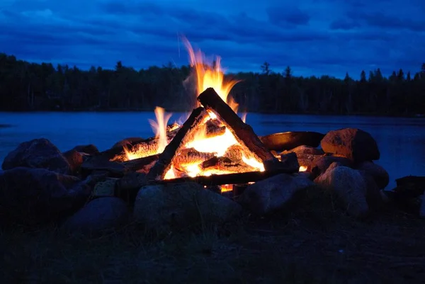 camp fire burning in a fire pit next to the lake