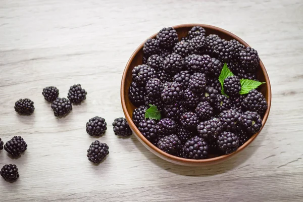 Ripe blackberries with leaves in a clay bowl on a light wooden background. Flat lay, top view. Photo of blackberry in clay bowl on wooden table. High resolution product. — Stock Photo, Image