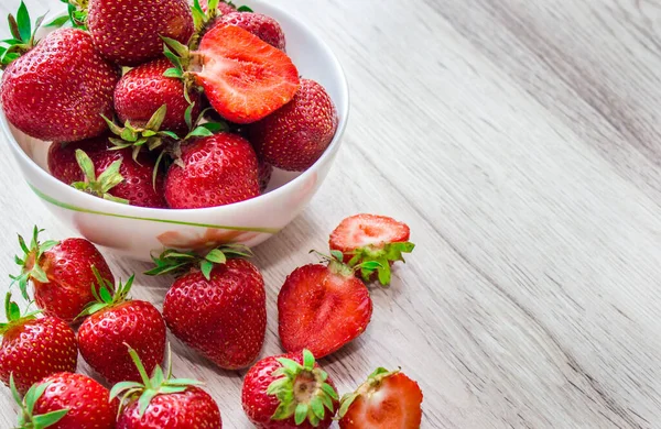 Montón de fresas frescas en un tazón de cerámica negra sobre fondo rústico de madera blanca . — Foto de Stock