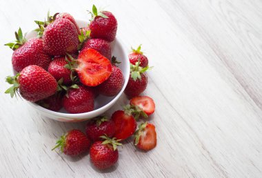 Kırsal beyaz ahşap arka planda seramik kasede taze çilek yığını.