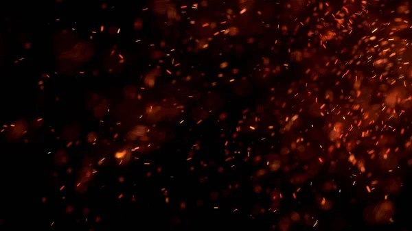 Gece gökyüzündeki büyük ateşten yanan kırmızı kıvılcımlar uçuşuyor. Ateş, ışık ve yaşam teması üzerine çok soyut bir arka plan. Yanan közler siyah arkaplan üzerinde uçan parçacıklar.