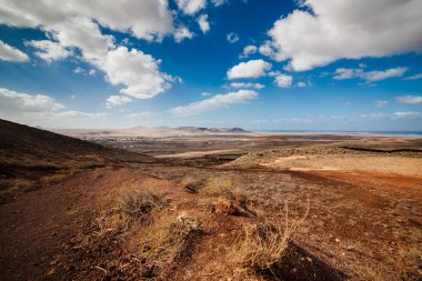 Dağları olan inanılmaz volkanik bir manzara. Gökyüzü bulutlarla mavidir, çakıllar kırmızı ve kahverengi. Fuerteventura Adası, Kanarya Adası, İspanya, Avrupa.