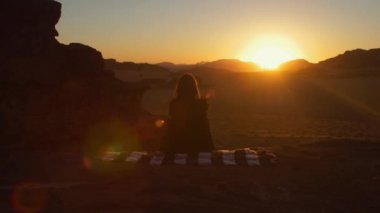 Çöl Wadi Rum Amazing Sunset, Kız halı üzerinde oturuyor ve o dinleniyor. Ürdün'de Kızıl Çöl Wadi Rum Manzara. 