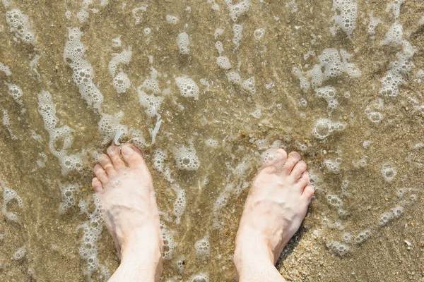 Asian Caucasian male feet on the sand with a wave comes in, on holiday.copy space.top view
