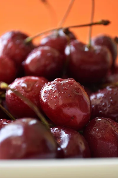 Ciliegie rosse fresche con gocce d'acqua su sfondo arancione . — Foto Stock