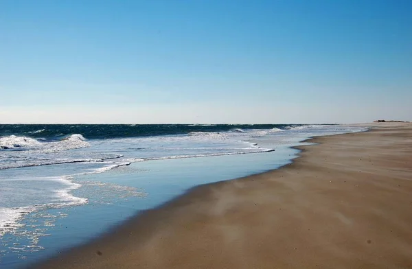 Bulutlu gökyüzünün altında kumda kırılan dalgalar.